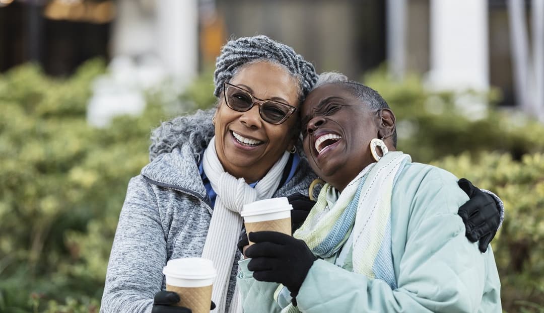 Two women laughing together over coffee outdoors